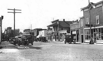 Street scene of Honor, MI in the early 1900s showing storefronts and parked Model T cards